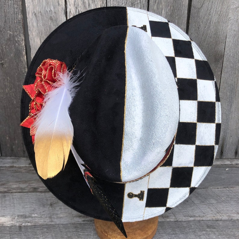 May include: A black and white checkered hat with a red and gold feather accent. The hat has a black crown and a white brim with a black and white checkered pattern.