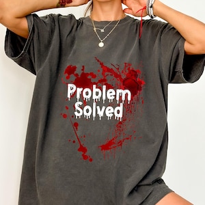 May include: Dark gray t-shirt with the text "Problem Solved" in white, surrounded by a splatter design in red. The shirt has short sleeves and a relaxed fit.