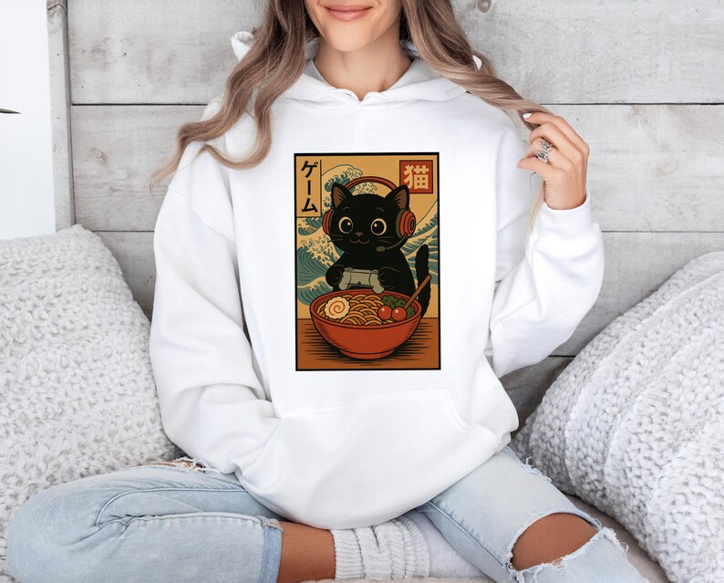 May include: White hoodie featuring a graphic of a black cat wearing headphones and playing a video game, with a bowl of ramen. The design has Japanese text and a wave pattern background.