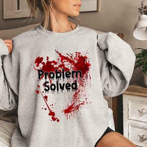 Może przedstawiać: Jasnoszara bluza z napisem "Problem Solved" w kolorze czarnym, z czerwonym wzorem rozprysk&oacute;w. Wz&oacute;r znajduje się na przodzie bluzy z długim rękawem i okrągłym dekoltem.