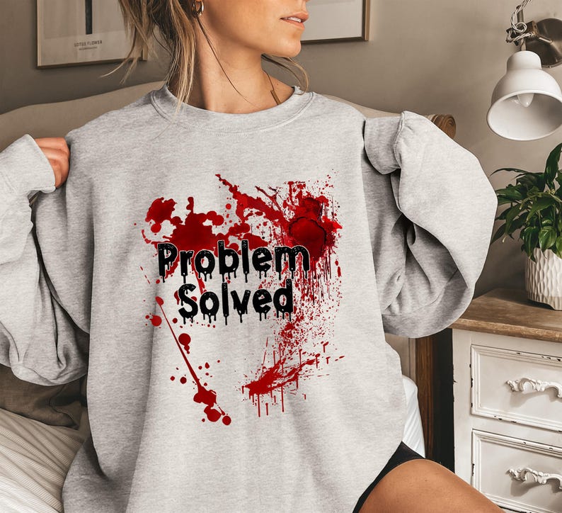 Może przedstawiać: Jasnoszara bluza z napisem "Problem Solved" w kolorze czarnym, z czerwonym wzorem rozprysk&oacute;w. Wz&oacute;r znajduje się na przodzie bluzy z długim rękawem i okrągłym dekoltem.