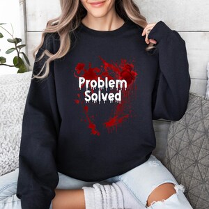 Może przedstawiać: Czarna bluza z białym napisem "Problem Solved" w kroplowym kroju pisma. Tekst jest nałożony na czerwony wz&oacute;r rozprysk&oacute;w. Bluza ma swobodny styl.