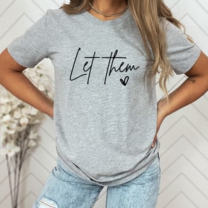 May include: A gray t-shirt with the text "Let them" in black cursive lettering and a small heart symbol.