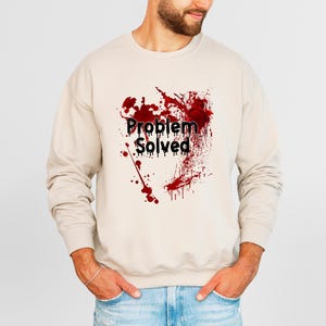 Może przedstawiać: Beżowa bluza z napisem "Problem Solved" w kolorze czarnym, nałożonym na czerwony wz&oacute;r rozprysk&oacute;w. Bluza w stylu casual, odpowiednia do noszenia na co dzień.