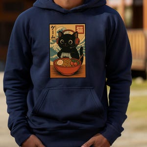 May include: Navy blue hoodie featuring a graphic of a black cat wearing headphones and playing a video game, with a bowl of ramen. The graphic includes Japanese text and a wave design. The hoodie has a front pocket and a drawstring hood.