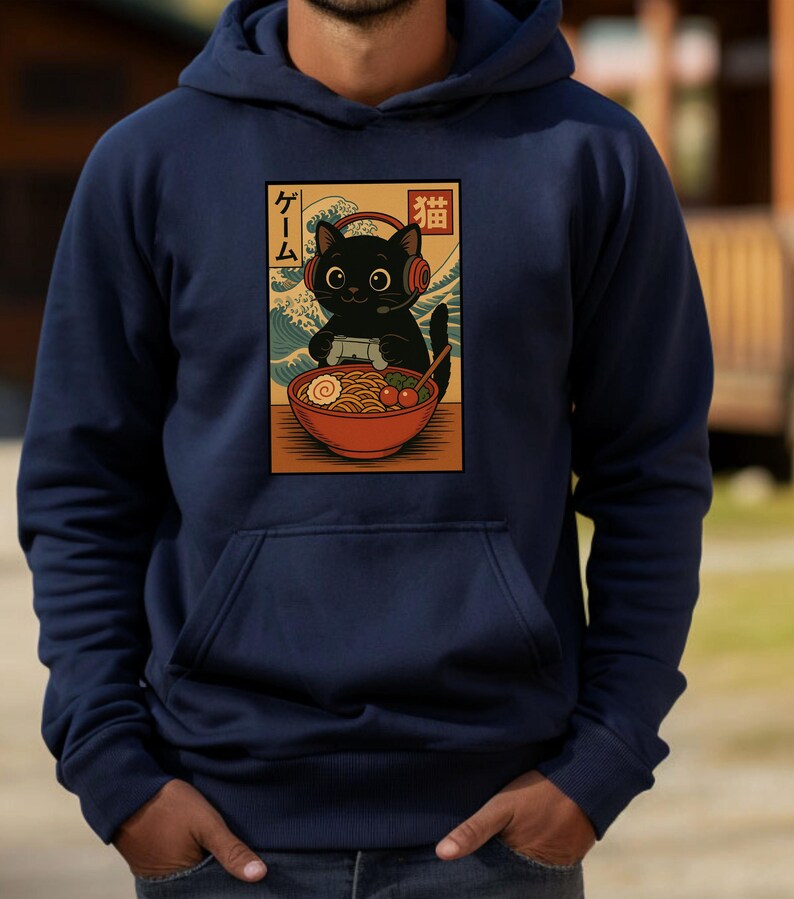 May include: Navy blue hoodie featuring a graphic of a black cat wearing headphones and playing a video game, with a bowl of ramen. The graphic includes Japanese text and a wave design. The hoodie has a front pocket and a drawstring hood.