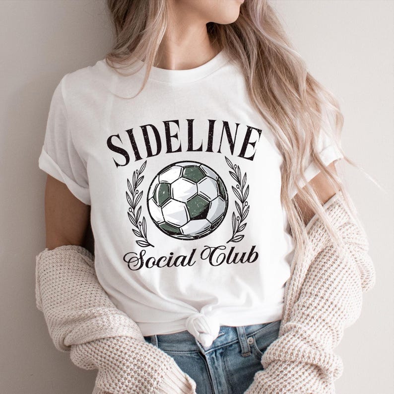 White shirt with “Sideline Social Club” text surrounding a soccer ball framed by laurel leaves. Retro sports design for moms, fans, and soccer families.