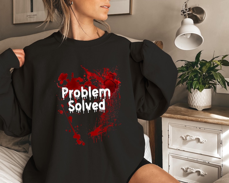 Może przedstawiać: Czarna bluza z białym napisem "Problem Solved" w kroplowym kroju pisma, na tle czerwonego wzoru rozprysk&oacute;w. Bluza ma długie rękawy i okrągły dekolt.