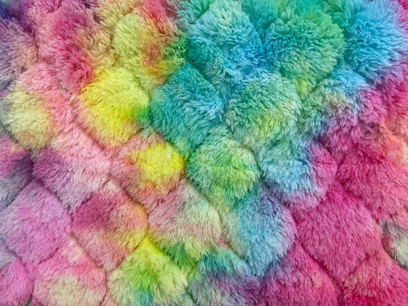 May include: Close-up of a soft, textured fabric in a vibrant rainbow of colors. The plush material features a repeating pattern of diamond-shaped tufts, with hues of pink, yellow, green, and blue blending together. The overall effect is a colorful and cozy textile.