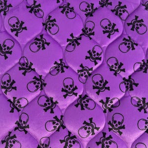 May include: Purple fabric with a repeating pattern of black skull and crossbones.