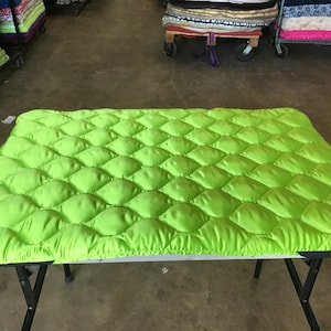 May include: A bright green quilted fabric with a diamond pattern. The fabric is laid flat on a folding table.