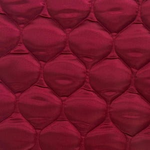 Puede incluir: Primer plano de una tela acolchada de color rojo intenso. La tela tiene un patrón de diamante con una textura en relieve.