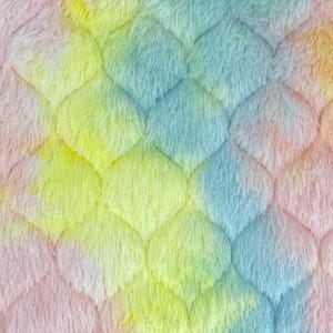 May include: A plush, faux fur fabric featuring a quilted, scalloped pattern. The material displays a tie-dye color palette of soft pastel pink, yellow, and light blue, creating a multi-colored, textured surface with a dense, fuzzy pile.