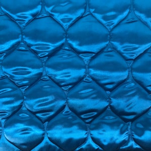 May include: A close-up of a quilted fabric with a teal blue color. The fabric has a diamond pattern with a raised, shiny texture.