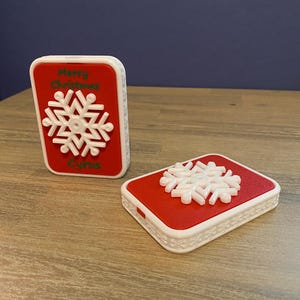 May include: Two red and white 3D printed ornaments with a white snowflake design. The top ornament has the text "Merry Christmas" and "Cirus" printed on it.