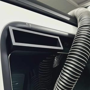 May include: A section of a vehicle's exterior, predominantly white and black. A flexible, ribbed hose with black and white stripes emerges from the vehicle's frame. A rectangular black panel with a silver trim is also visible.