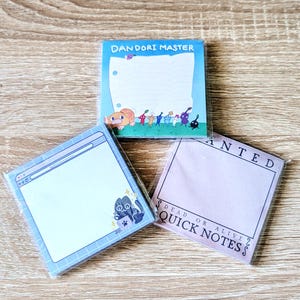 May include: Three square sticky note pads in clear plastic packaging. One features Pikmin characters and the text DANDORI MASTER. Another shows a blue computer window interface with a cat. The third is a light purple WANTED DEAD OR ALIVE note pad.