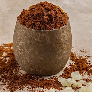 May include: A dark brown, rounded stone bowl filled to the brim with a mound of fine, reddish-brown powder. Scattered around the base of the bowl are several small, translucent, pale yellow resinous chunks with irregular, jagged edges.