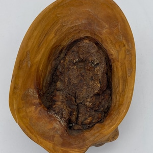 Op de afbeelding: Een kleine houten kom met een natuurlijke, rustieke afwerking. De kom is gesneden uit één stuk hout en heeft een unieke, organische vorm.