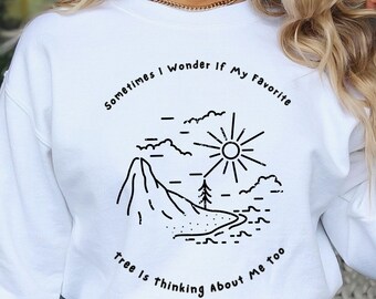 Può includere: Felpa bianca con un design grafico nero di una montagna, un sole e un albero. Il testo recita "Sometimes I wonder if my favorite tree is thinking about me too."