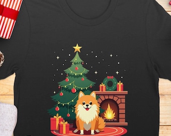 May include: A black t-shirt with a Christmas-themed design featuring a small orange and white dog sitting in front of a fireplace with a decorated Christmas tree and presents.