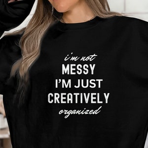 May include: Black sweatshirt with white text that reads "i'm not messy i'm just creatively organized"