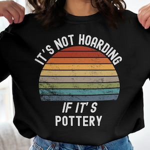 May include: Black sweatshirt with a vintage-style sunset graphic and the text "It's not hoarding if it's pottery."
