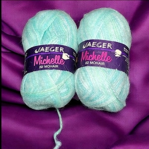 May include: Two skeins of light blue yarn with a white shimmer. The yarn is labeled "Jaeger Michelle with Mohair".