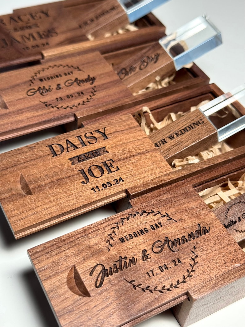 May include: Wooden boxes with engraved wedding details and dates. Each box contains a clear USB drive with a crystal-like appearance. The boxes are made of a rich brown wood with a natural grain pattern.