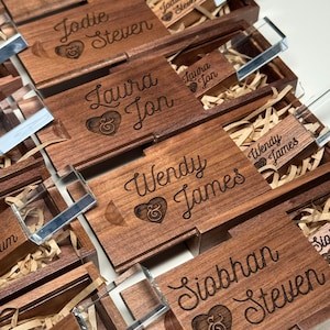 May include: A set of wooden boxes with engraved names and a heart symbol. Each box contains a clear acrylic USB drive.