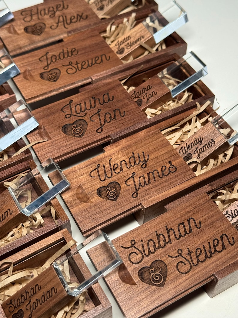 May include: A set of wooden boxes with engraved names and a heart symbol. Each box contains a clear acrylic USB drive.