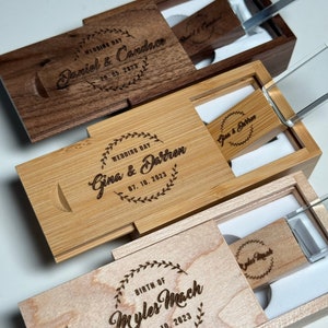 May include: Three wooden boxes with engraved text and clear glass lids. Each box contains a USB drive with a personalized inscription. The inscriptions include "Wedding Day Daniel & Candace 29.05.2023", "Wedding Day Gina & Darren 07.10.2023", and "Birth of Myles Mach 29.10.2023".