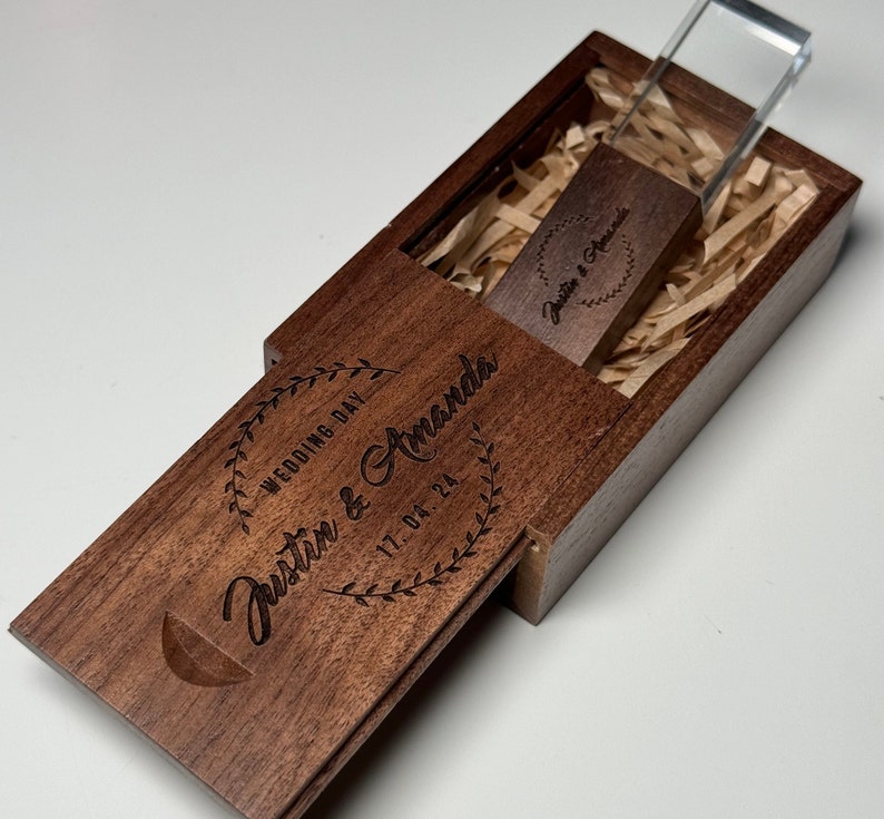 May include: A wooden box with a clear acrylic lid, containing a USB drive with the text "Justin & Amanda" and the date "17.04.24" engraved on it. The box is also engraved with the text "Wedding Day Justin & Amanda 17.04.24".