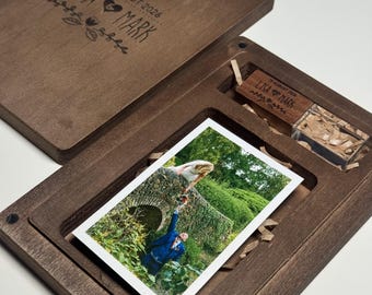 May include: A dark brown wooden keepsake box with a sliding lid engraved with the text LISA & MARK and 15 AUGUST 2026. The box contains a rectangular photograph of a couple and a small wooden USB drive engraved with the same text and date.