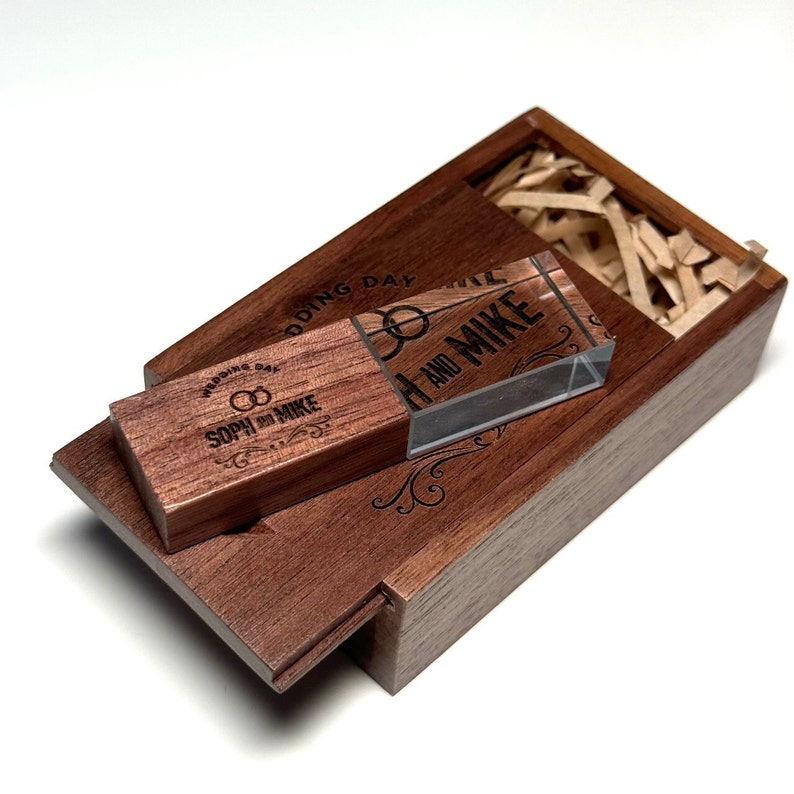 May include: A wooden box with a hinged lid, containing a clear acrylic USB drive with the text "SOPH & MIKE WEDDING DAY" engraved on the wooden part and "SOPH AND MIKE" engraved on the acrylic part.
