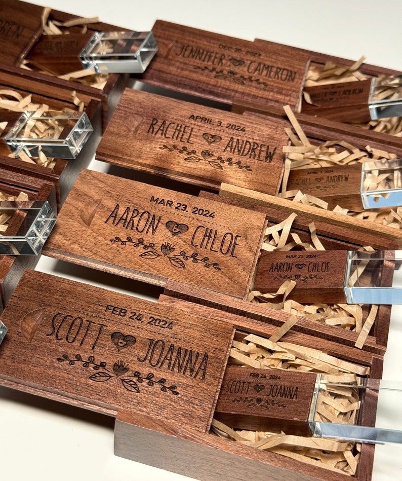 May include: Wooden boxes with engraved names and dates, each containing a crystal USB drive. The boxes are stacked on top of each other, with the top box open to reveal the USB drive inside.