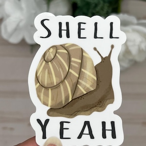 May include: A white sticker with a brown snail illustration and the text "SHELL YEAH" in black.