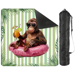 May include: A square outdoor blanket featuring a brown monkey wearing leopard-print sunglasses, sitting in a pink inflatable ring while holding a tropical drink with a lime slice and umbrella, set against a light green and white striped background.