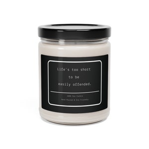 Puede incluir: Una vela de soja blanca en un tarro de vidrio con tapa negra. La etiqueta en el tarro dice "Life's too short to be easily offended." y "100% Soy Candle Hand Poured & Eco Friendly."