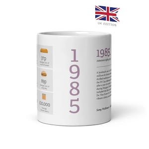 Puede incluir: Taza de cerámica blanca con un diseño 1985 morado. La taza presenta una línea de tiempo de eventos de 1985, incluyendo el costo promedio de una hogaza de pan, una Big Mac y el salario anual promedio. El texto "UK Edition" está impreso en la esquina superior derecha.
