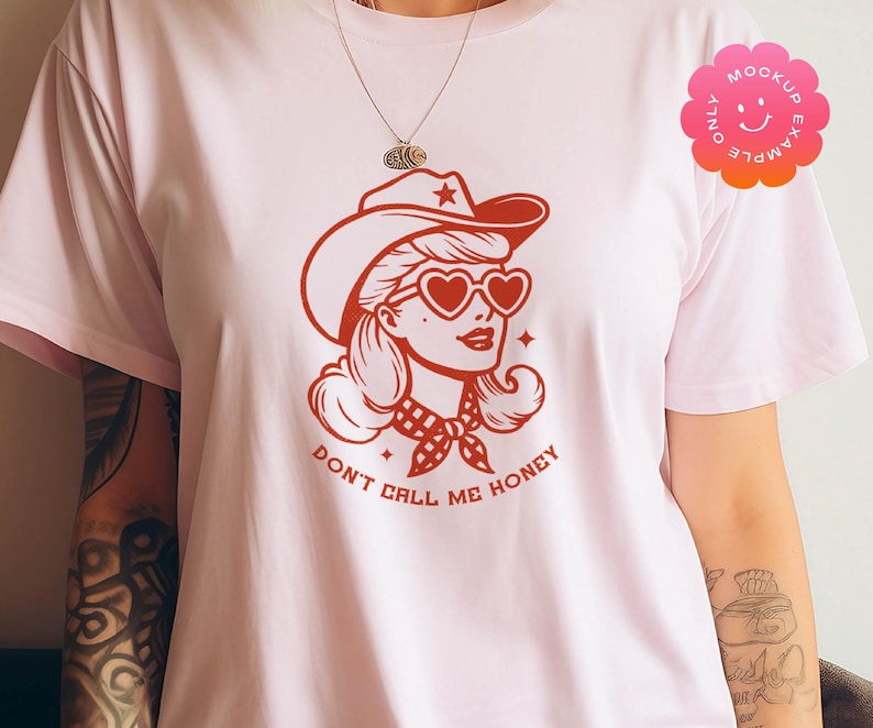 May include: Pink t-shirt with a red graphic of a woman wearing a cowboy hat and heart-shaped sunglasses. The text "Don't Call Me Honey" is printed below the graphic.
