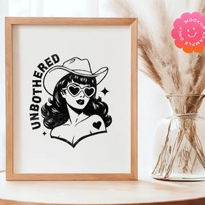 May include: A framed print with a black and white illustration of a woman wearing a cowboy hat and sunglasses. The text "UNBOTHERED" is written in a vintage style font.