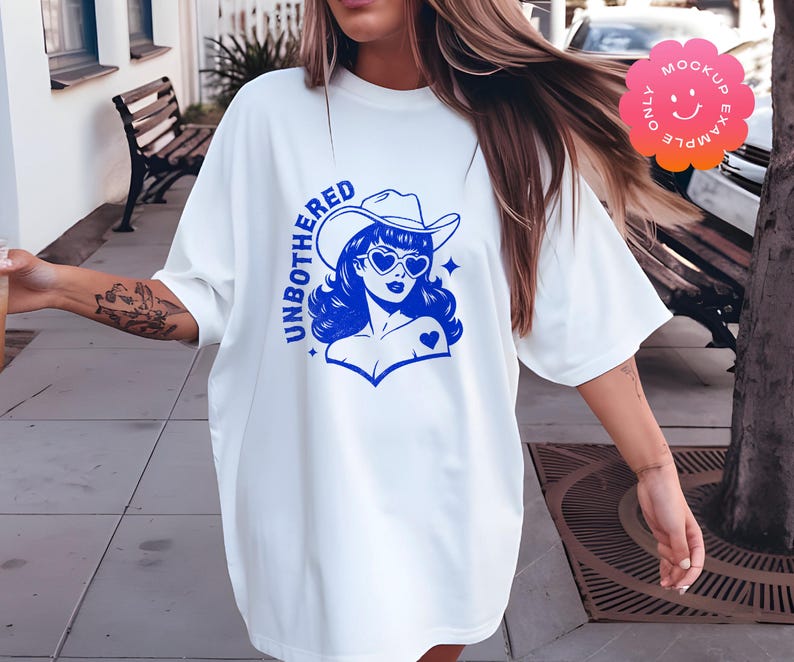 May include: White oversized t-shirt with a blue graphic of a woman wearing a cowboy hat and sunglasses. The graphic says "UNBOTHERED" in blue letters.