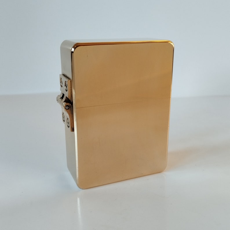 Op de afbeelding: Een gouden metalen doos met een scharnierend deksel. De doos heeft een eenvoudig ontwerp en is gemaakt van massief metaal.