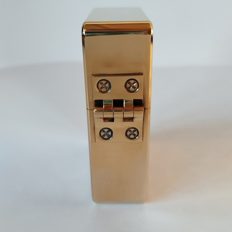 Op de afbeelding: Een gouden metalen doos met een scharnier en vier schroeven. De doos is gesloten.