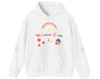 Può includere: Felpa con cappuccio bianca con un arcobaleno, sole, nuvole, fiori, api e un disegno di una casa. Il testo "Welcome Home" è stampato sul davanti della felpa.