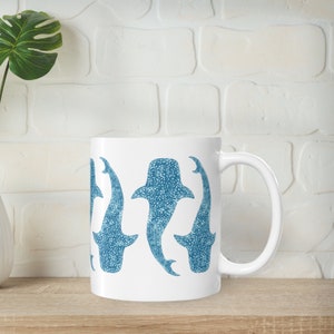 May include: White ceramic mug with a blue and white pattern of whale sharks. The mug has a handle on the right side.
