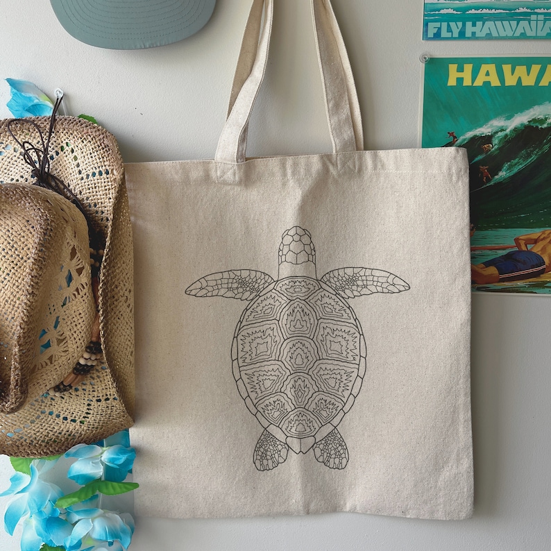 May include: A white canvas tote bag featuring a black line drawing of a sea turtle on the front. The turtle has a detailed shell design.