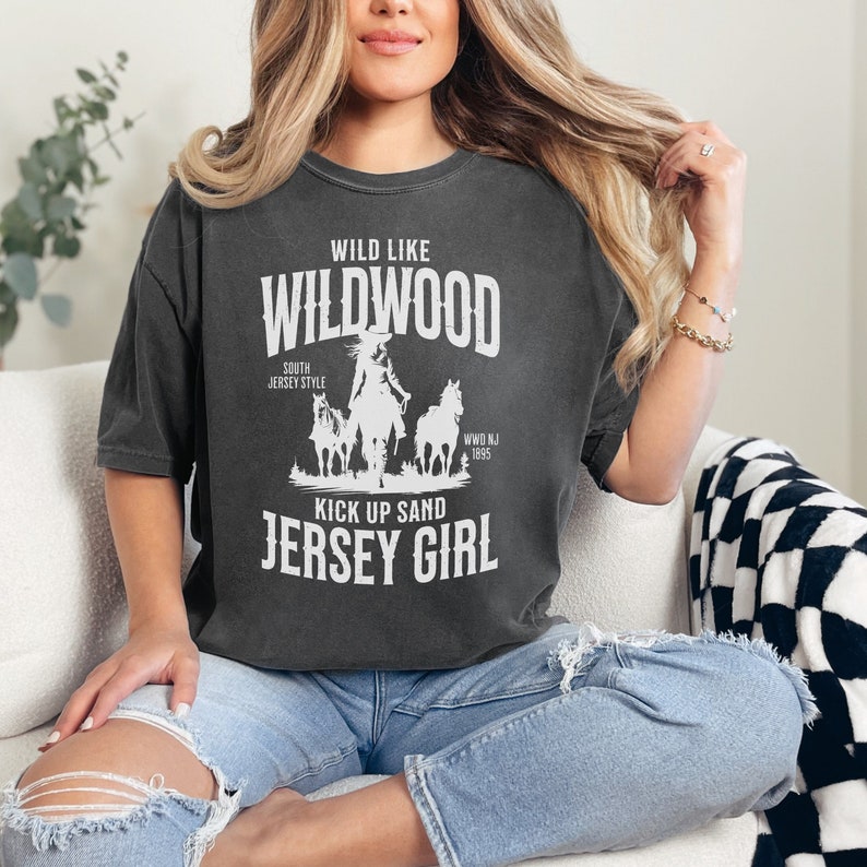 May include: A dark gray t-shirt with a white graphic design that says "Wild Like Wildwood South Jersey Style Kick Up Sand Jersey Girl" with a silhouette of a woman riding a horse.