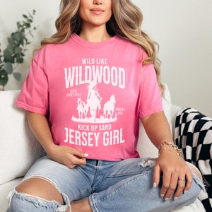 May include: A pink t-shirt with a white graphic that says "Wild Like Wildwood South Jersey Style Kick Up Sand Jersey Girl" with a silhouette of a woman riding a horse.